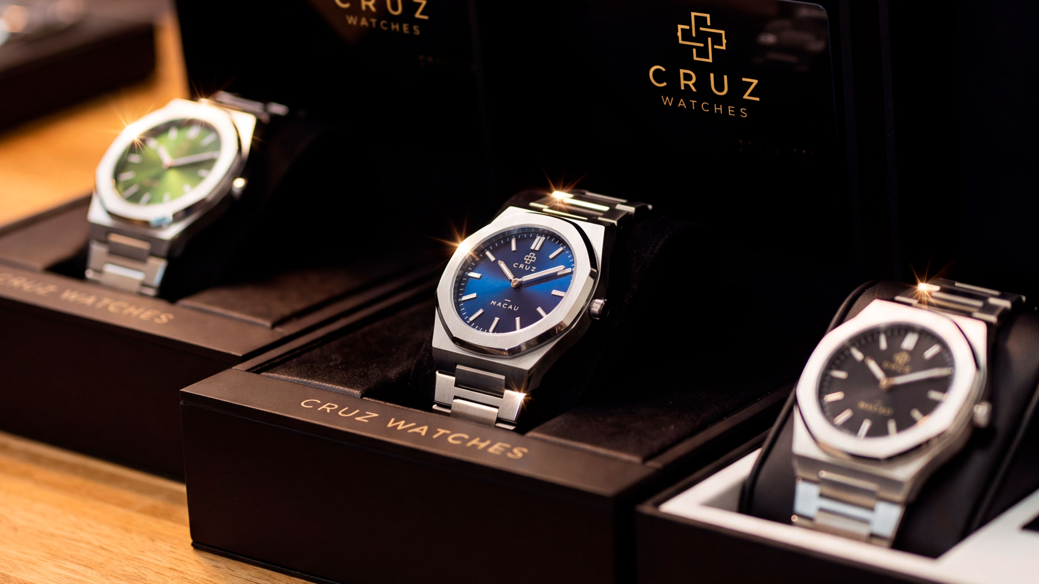 Três relógios Cruz Watches Macau, nas cores verde, azul e preto, apresentados em suas caixas.
